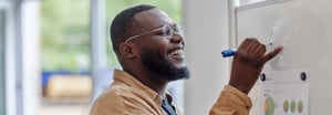 A smiling man writing with a marker on a white board