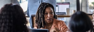 Woman of color in rust colored blouse in deep conversation with colleagues