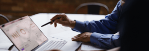 A man with a pen pointing at a laptop with data on it