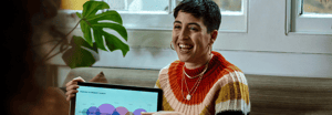 A smiling woman holding a tablet displaying a product launch roadmap chart during a casual meeting.