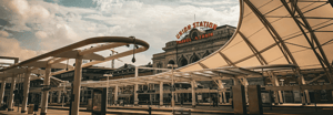 The exterior of Denver Union Station with its iconic neon sign, framed by modern transit canopy structures under a dramatic cloudy sky.