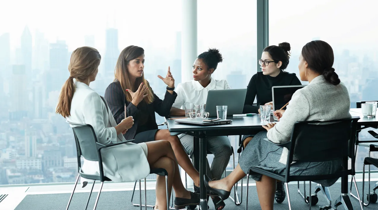 A team of women discuss a project around a conference room table. 